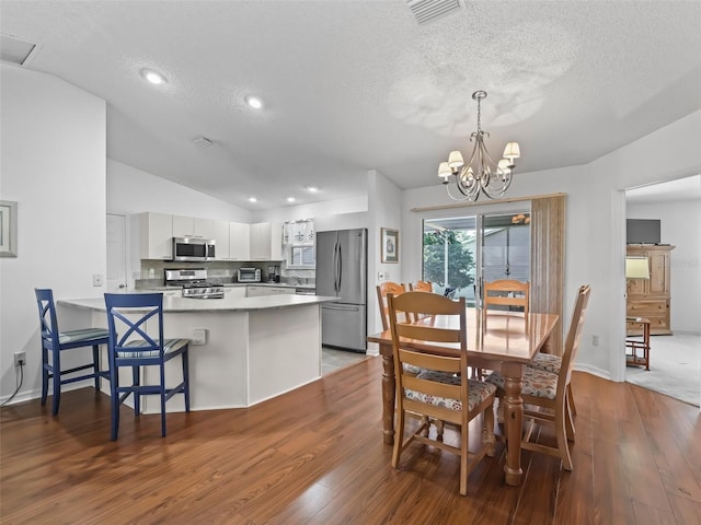 dining space with visible vents, wood finished floors, vaulted ceiling, a textured ceiling, and a notable chandelier