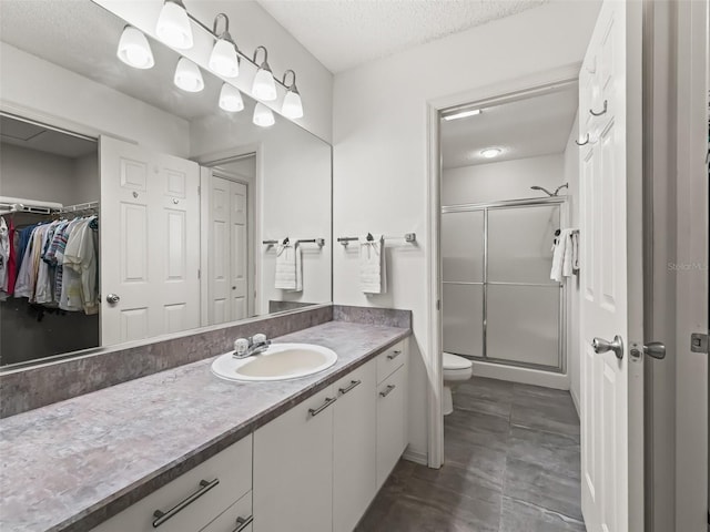 bathroom with a textured ceiling, toilet, vanity, a spacious closet, and a shower stall