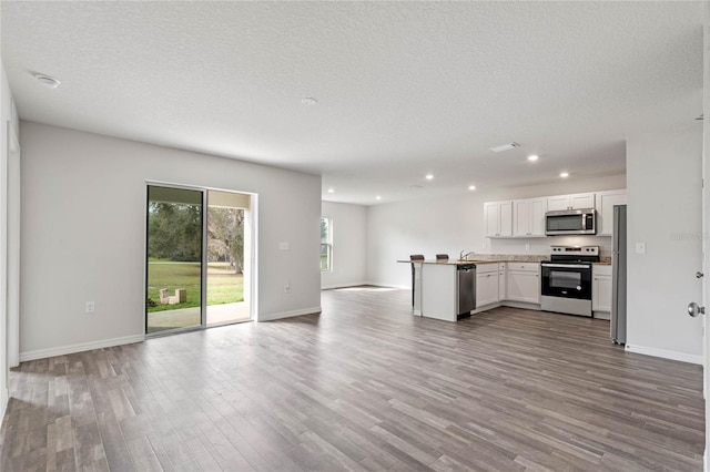 kitchen featuring appliances with stainless steel finishes, open floor plan, white cabinetry, and wood finished floors