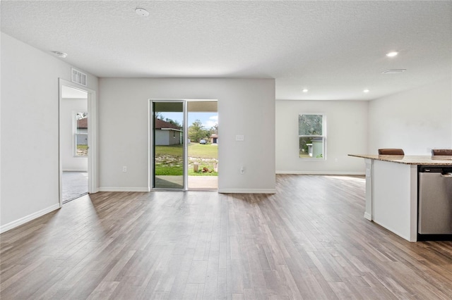 unfurnished living room featuring visible vents, a textured ceiling, baseboards, and wood finished floors