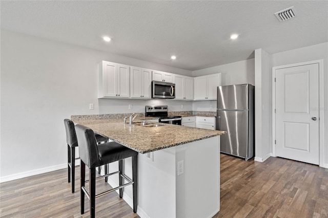 kitchen with a peninsula, a sink, visible vents, appliances with stainless steel finishes, and light stone countertops