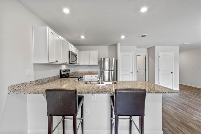 kitchen with a kitchen breakfast bar, wood finished floors, a peninsula, stainless steel appliances, and a sink