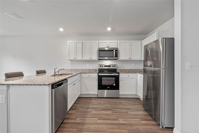 kitchen with a peninsula, wood finished floors, a sink, visible vents, and appliances with stainless steel finishes