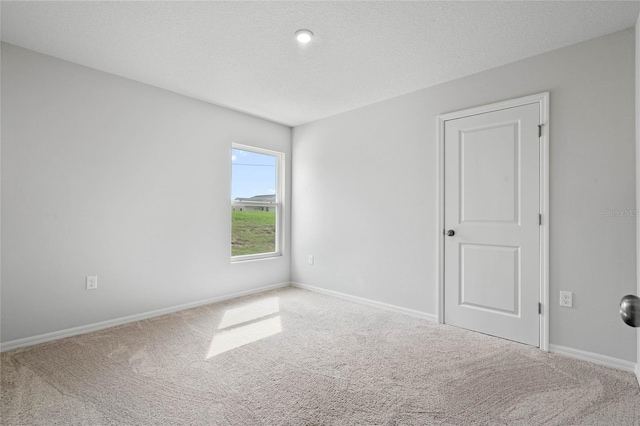 empty room featuring a textured ceiling, carpet flooring, and baseboards