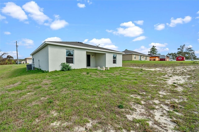 rear view of property featuring a lawn, cooling unit, and stucco siding