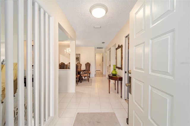 corridor featuring light tile patterned floors, a textured ceiling, and an inviting chandelier