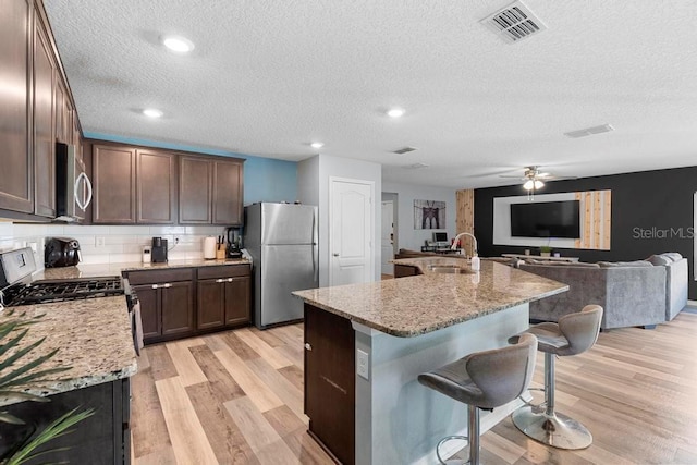 kitchen featuring a breakfast bar, stainless steel appliances, visible vents, light wood-style floors, and a sink