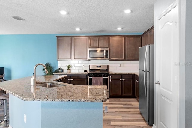 kitchen with a sink, visible vents, appliances with stainless steel finishes, light stone countertops, and light wood finished floors