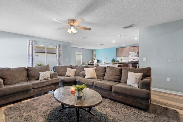 living area featuring visible vents, a ceiling fan, a textured ceiling, wood finished floors, and baseboards