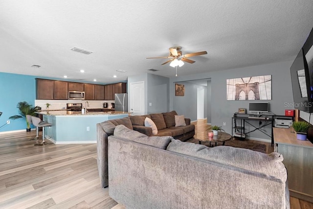 living area with visible vents, ceiling fan, a textured ceiling, and light wood-style flooring