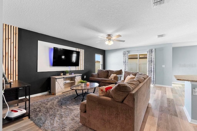 living room featuring light wood finished floors, baseboards, visible vents, and ceiling fan