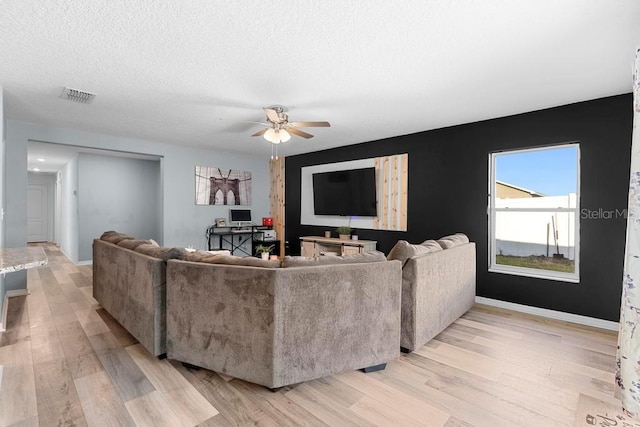 living area featuring light wood-style floors, baseboards, visible vents, and a textured ceiling