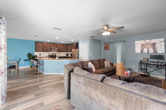 living room featuring visible vents, baseboards, light wood-style flooring, ceiling fan, and a textured ceiling