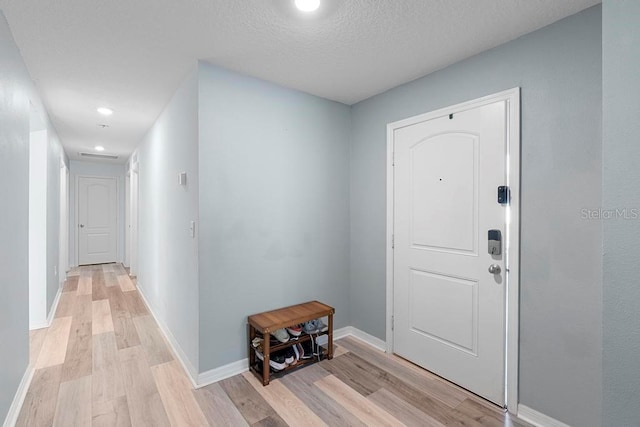 foyer entrance featuring a textured ceiling, light wood finished floors, and baseboards