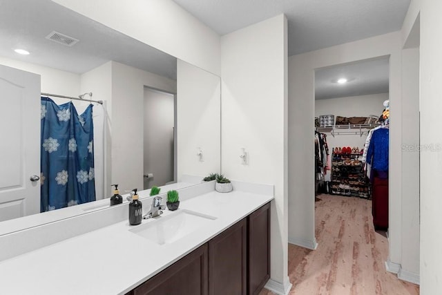 full bath featuring recessed lighting, visible vents, a spacious closet, vanity, and wood finished floors