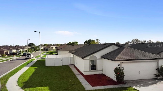 view of property exterior with a garage, fence, driveway, a lawn, and a residential view