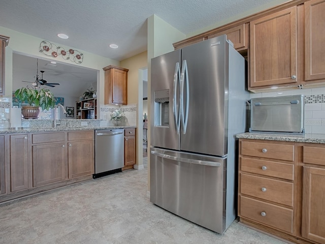 kitchen featuring light stone counters, backsplash, appliances with stainless steel finishes, brown cabinetry, and a sink