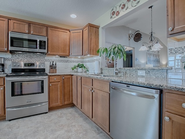 kitchen featuring light stone counters, brown cabinets, stainless steel appliances, backsplash, and a sink