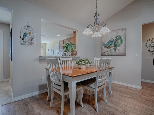 dining room with light wood-type flooring, vaulted ceiling, a textured ceiling, and baseboards