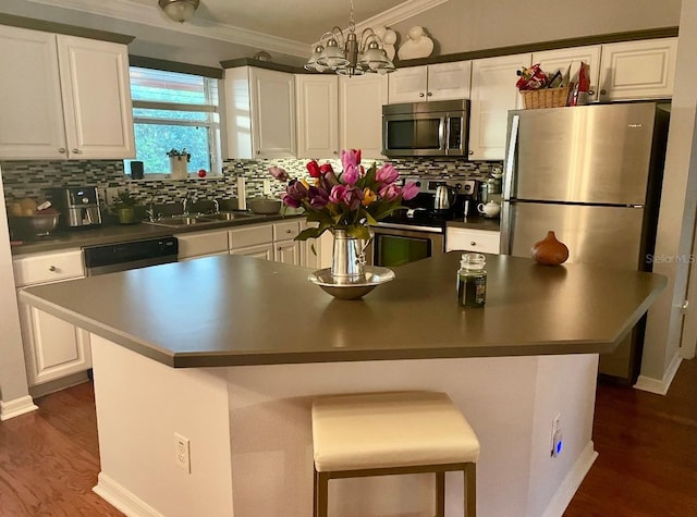 kitchen featuring stainless steel appliances, a sink, white cabinets, ornamental molding, and dark countertops