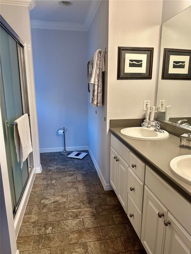 bathroom featuring double vanity, a stall shower, baseboards, crown molding, and a sink