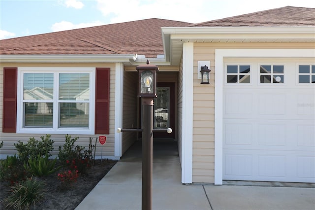 doorway to property with a garage and a shingled roof