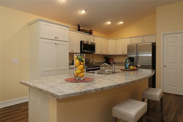 kitchen with vaulted ceiling, appliances with stainless steel finishes, a sink, and white cabinets