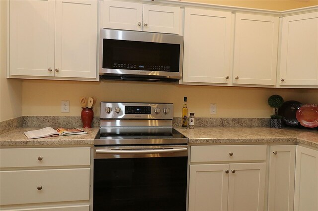 kitchen featuring stainless steel appliances, white cabinets, and light countertops