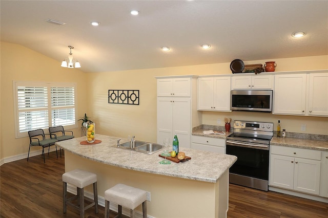 kitchen with appliances with stainless steel finishes, white cabinets, vaulted ceiling, a sink, and a kitchen breakfast bar