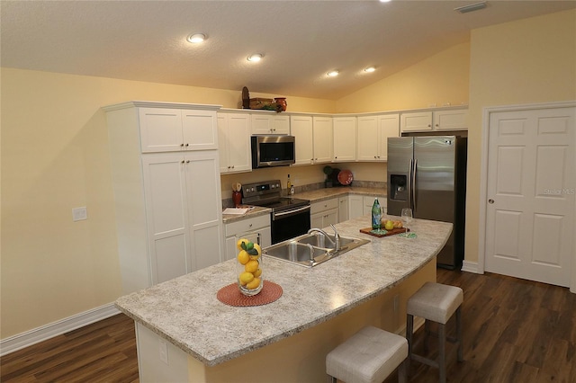 kitchen featuring a sink, white cabinetry, a kitchen breakfast bar, vaulted ceiling, and appliances with stainless steel finishes