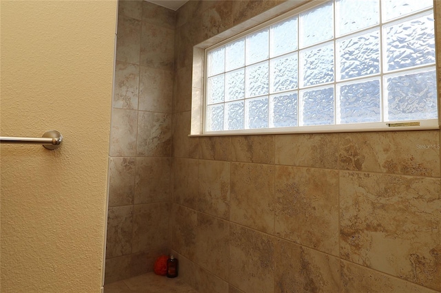 full bath featuring a tile shower and a textured wall