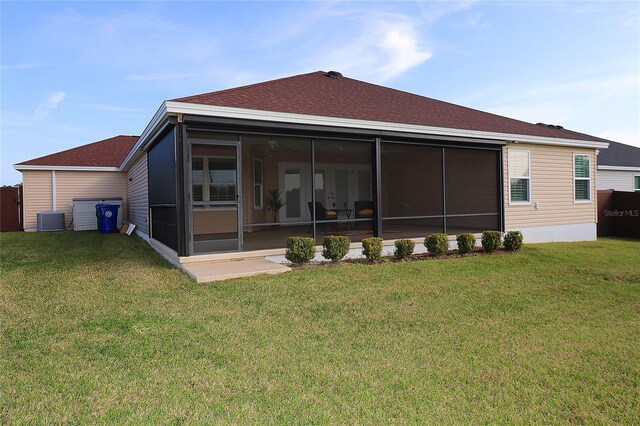 rear view of property featuring a yard, central AC unit, a shingled roof, and a sunroom