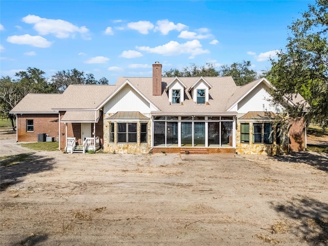 back of property featuring a sunroom, a chimney, metal roof, roof with shingles, and a standing seam roof