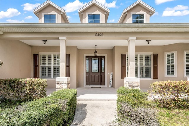 view of exterior entry with stone siding, a porch, and stucco siding