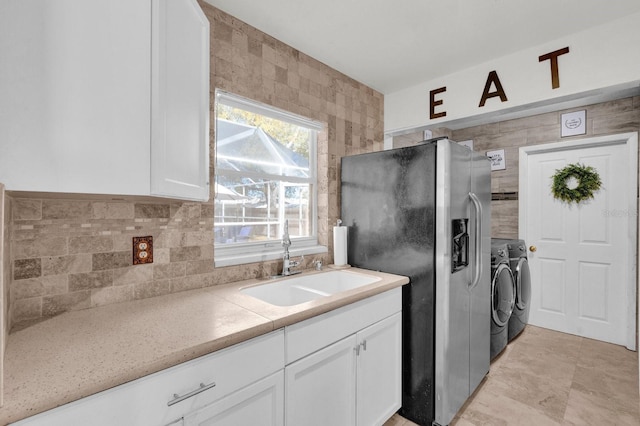 kitchen with stainless steel refrigerator with ice dispenser, washer and clothes dryer, a sink, backsplash, and white cabinets