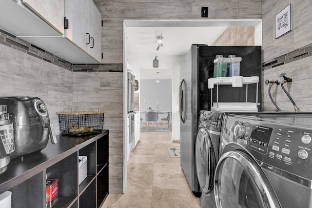 washroom with tile walls, cabinet space, and washer and clothes dryer