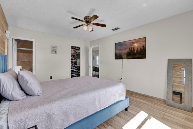 bedroom with a walk in closet, wood finished floors, visible vents, and a textured ceiling