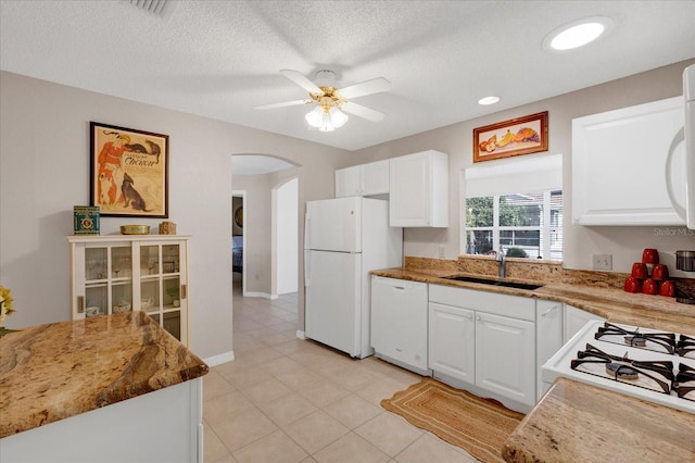 kitchen with arched walkways, white appliances, a sink, and white cabinetry