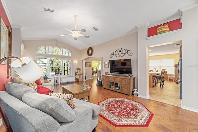 living area featuring lofted ceiling, visible vents, arched walkways, and ornamental molding