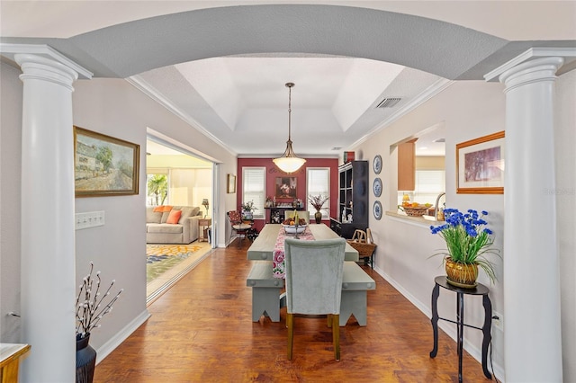 dining space featuring wood finished floors, a tray ceiling, decorative columns, and visible vents