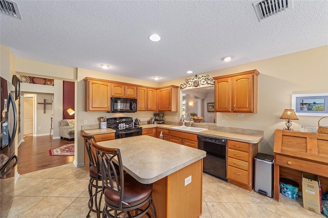 kitchen featuring a breakfast bar, light countertops, visible vents, a sink, and black appliances