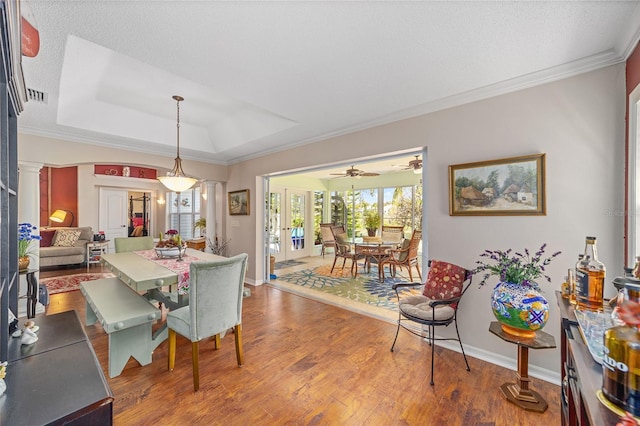 dining space with ornate columns, baseboards, a raised ceiling, and wood finished floors