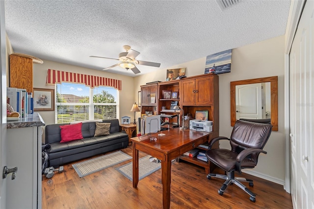 office featuring a textured ceiling, visible vents, baseboards, a ceiling fan, and dark wood finished floors