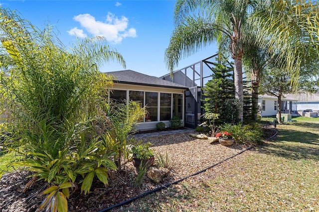 back of property featuring a shingled roof, glass enclosure, and a yard