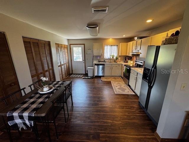 kitchen featuring visible vents, appliances with stainless steel finishes, dark wood-type flooring, light countertops, and under cabinet range hood