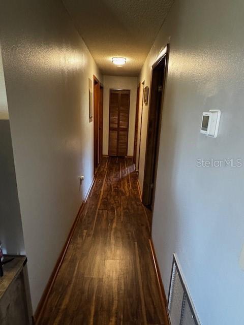 hall featuring dark wood-style floors, baseboards, visible vents, and a textured ceiling