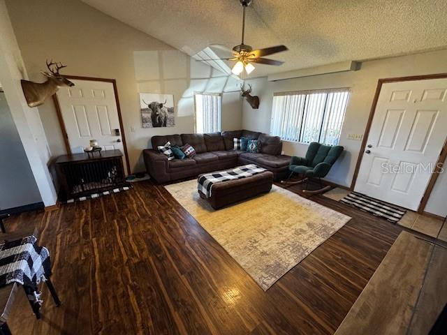 living area featuring lofted ceiling, ceiling fan, a textured ceiling, and wood finished floors