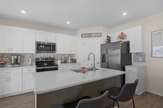 kitchen featuring a breakfast bar area, stainless steel appliances, wood finished floors, white cabinets, and light countertops