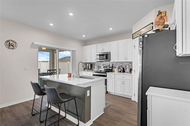 kitchen featuring tasteful backsplash, white cabinets, a kitchen breakfast bar, stainless steel appliances, and a sink