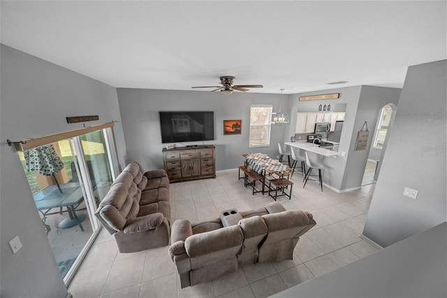 living area featuring a wealth of natural light, ceiling fan with notable chandelier, and light tile patterned floors